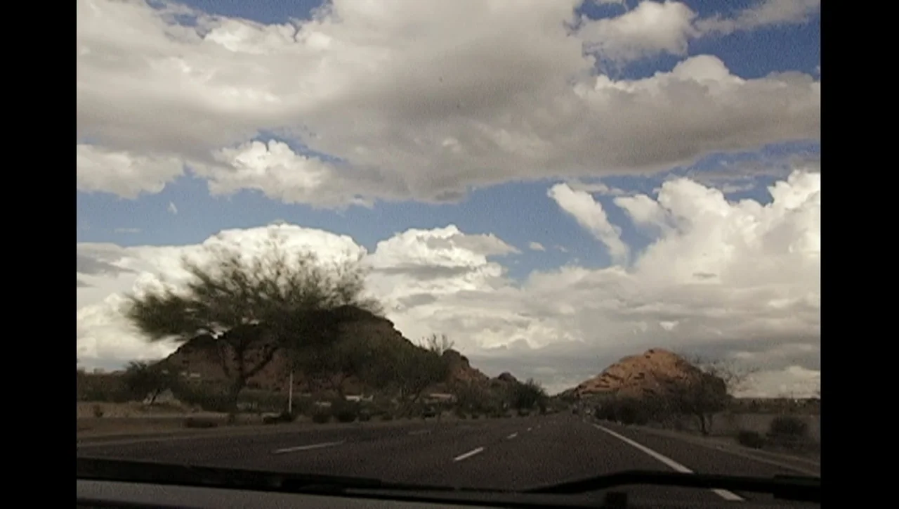 The Trials of Ted Haggard (2009) movie still: establishing — A paved asphalt highway leads toward two large dark rock formations under scattered…