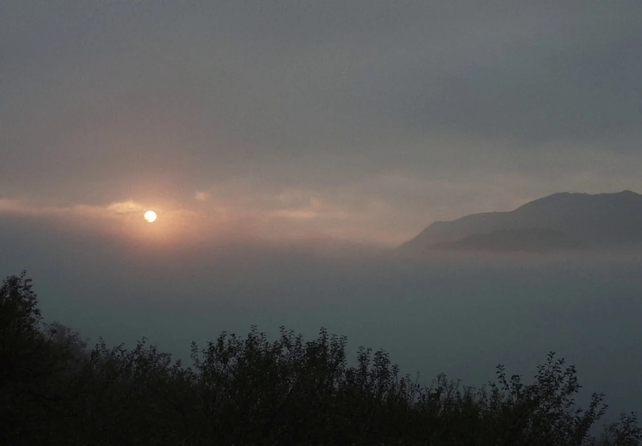 You Won’t Be Alone (2022) movie still: establishing — A dense blanket of fog rests against the silhouette of a mountain range at dawn. The pale sun…