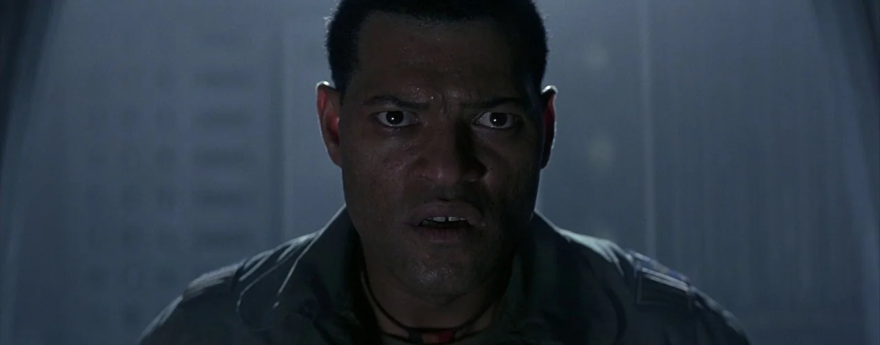Event Horizon (1997) movie still: closeup — A dimly lit interior space with metallic walls and cool blue illumination. A man stares forward with a…