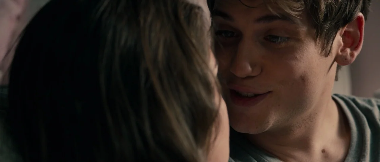 The Purge (2013) movie still: closeup — A close-up view shows two people in a darkened indoor setting. A man with short wavy hair looks at a woman…