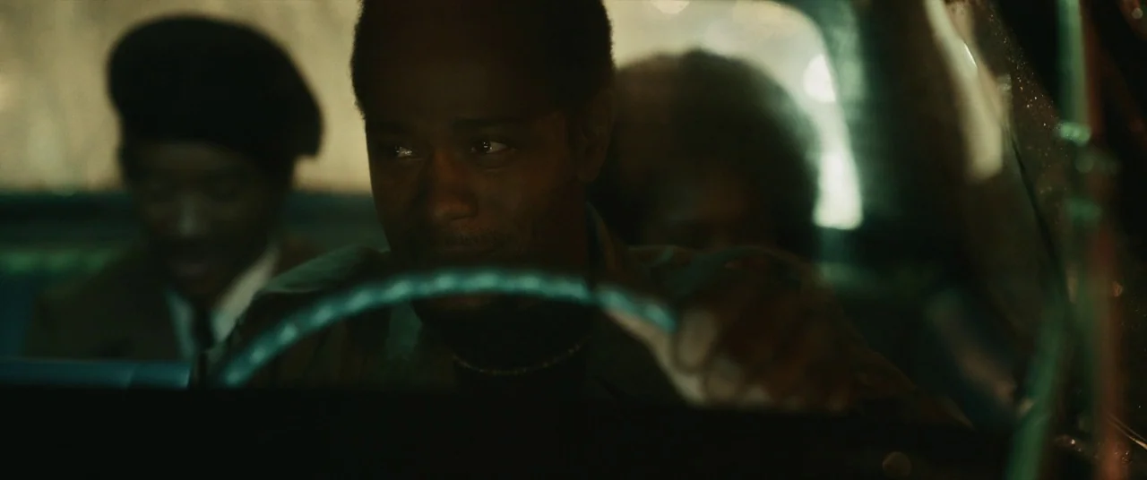 Judas and the Black Messiah (2021) movie still: medium — The interior of a vintage car at night illuminated by passing external streetlights. A man…