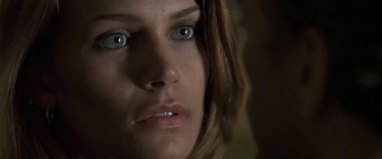 Maximum Risk (1996) movie still: closeup — A dimly lit interior room serves as the setting for two people. A woman in the foreground looks directly…