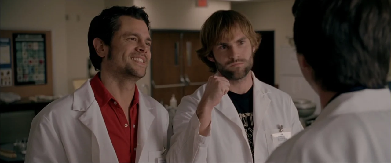 The Dukes of Hazzard (2005) movie still: medium — Two men in white lab coats stand in a well-lit medical facility office. The men face an off-screen…