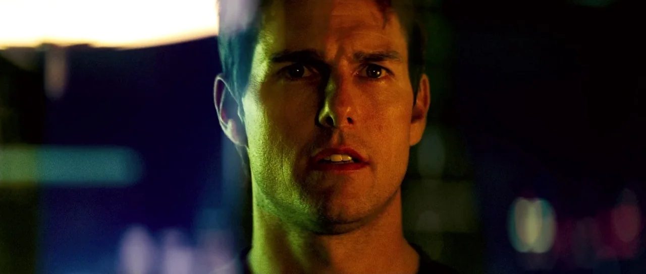 Mission: Impossible III (2006) movie still: closeup — A dark urban environment at night with blurred colored lights visible in the background. A man…