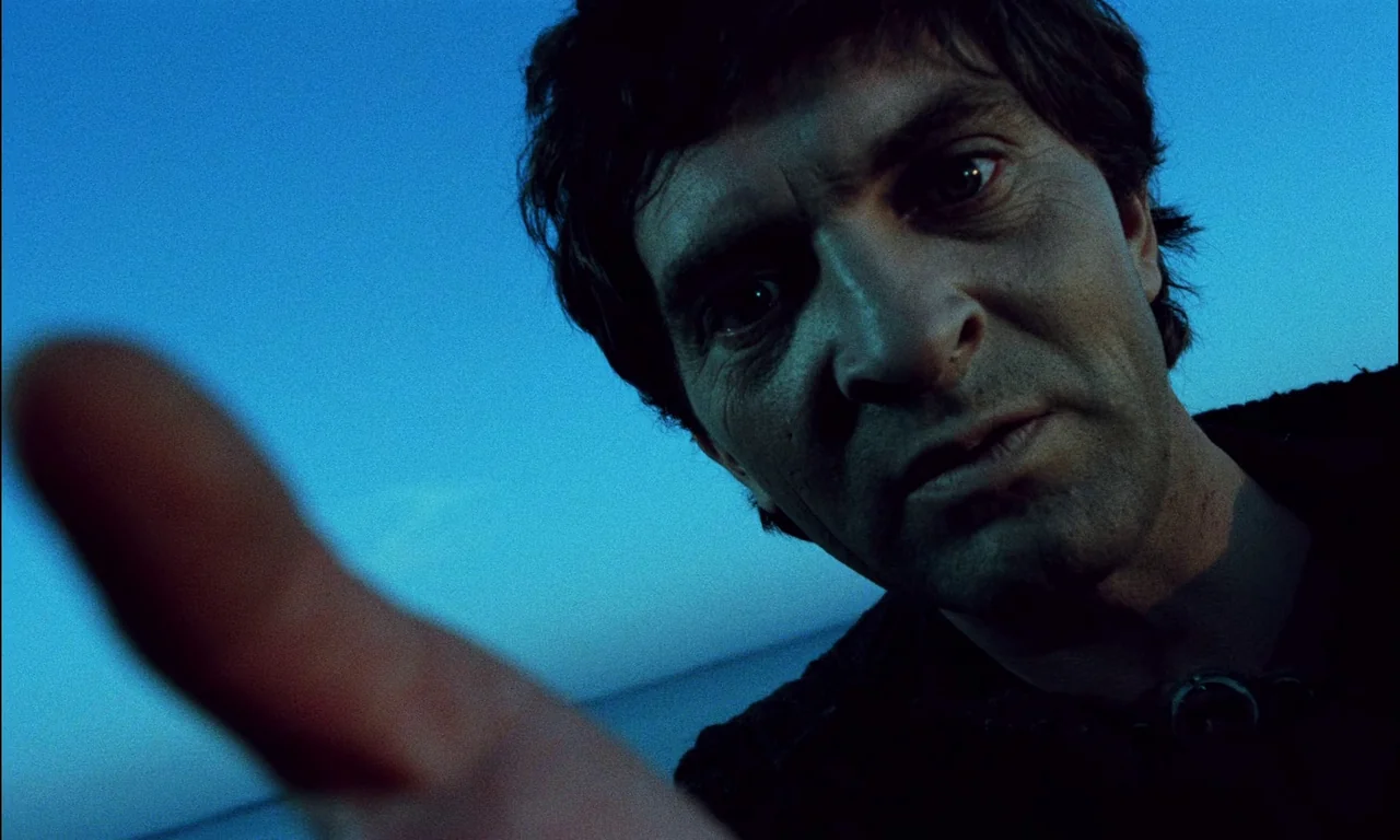 On The Silver Globe (1988) movie still: closeup — An open space under a deep blue twilight sky. A man leans down, reaching his hand toward the…