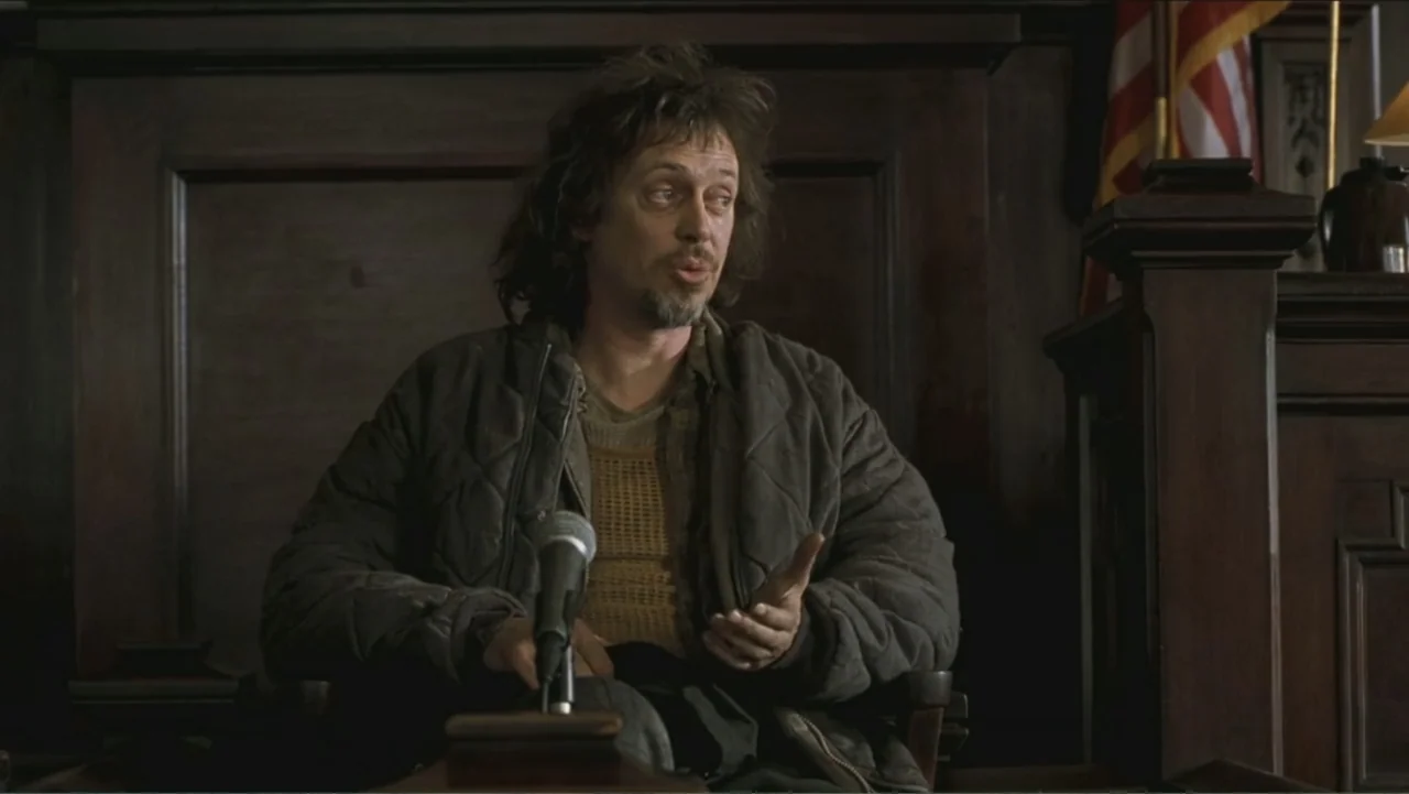 Big Daddy (1999) movie still: medium — A wooden witness stand features a built-in microphone in a dim, formal interior. A disheveled man sits in the…