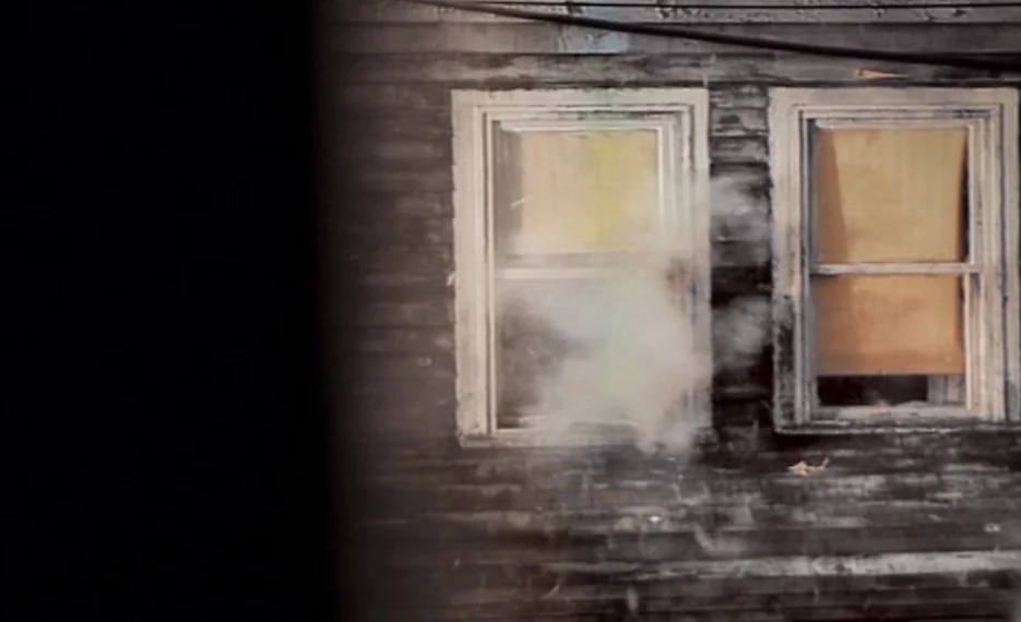 Dear Wendy (2005) movie still: medium — The exterior of a weathered house features dark horizontal wood siding and two rectangular windows. Thick…