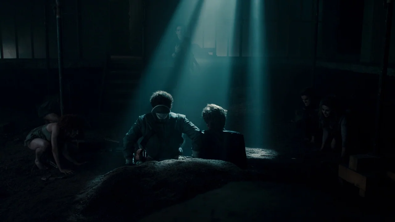 Fright Night (2011) movie still: wide — A dark subterranean space filled with piles of dirt and dust particles. Two men sit on the ground facing a…