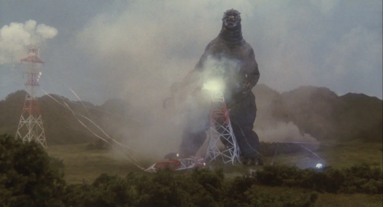 Godzilla vs. Mechagodzilla II (1993) movie still: wide — A giant reptilian creature stands within a grassy field surrounded by power transmission…