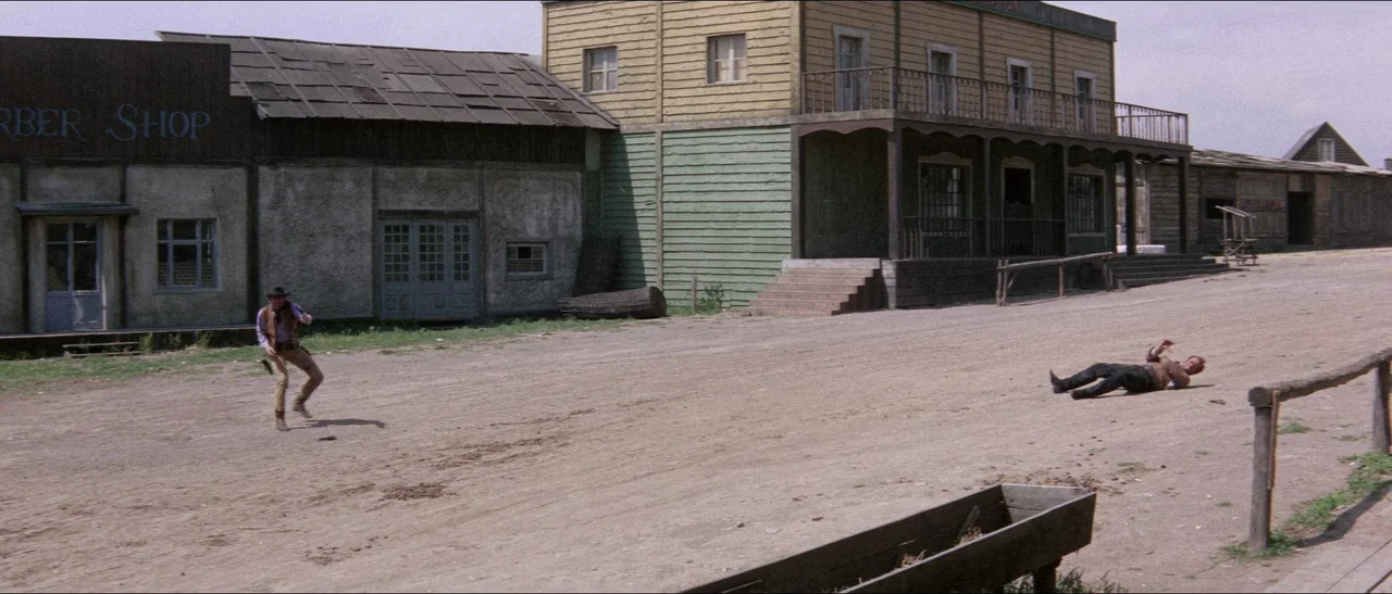 Texas, Adios (1966) movie still: wide — A dusty dirt street lined with weathered, wood-paneled storefronts and a saloon. One man stands with a…