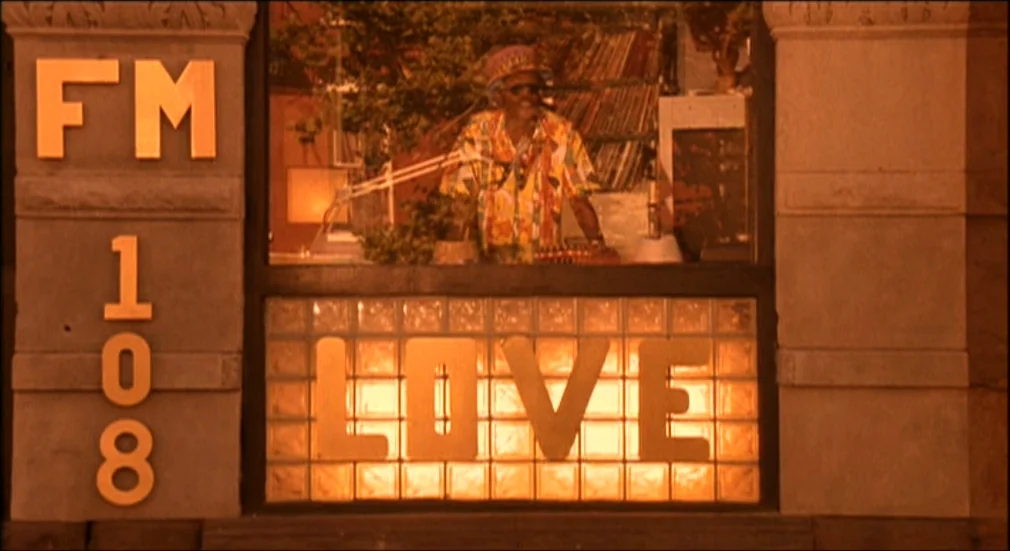 Do The Right Thing (1989) movie still: medium — A radio station booth exterior featuring gold lettering and glass block windows. An older man in a…
