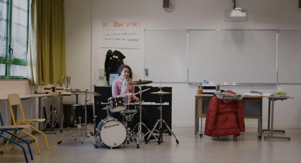 A Dramatic Film (2019) movie still: wide — A quiet room used for academic instruction with a whiteboard and desks arranged inside. A young person…