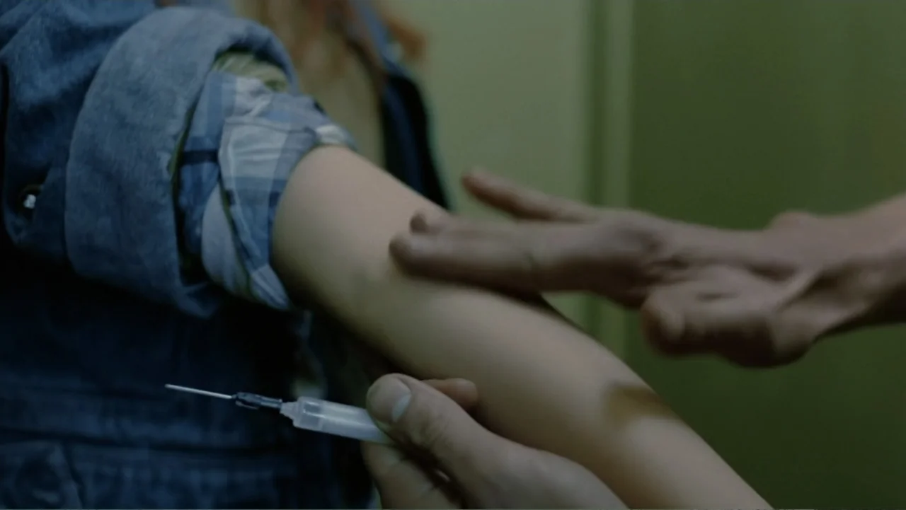 Christiane F. (1981) movie still: closeup — An interior space features a person preparing a hypodermic needle near an arm. A second person's hand…