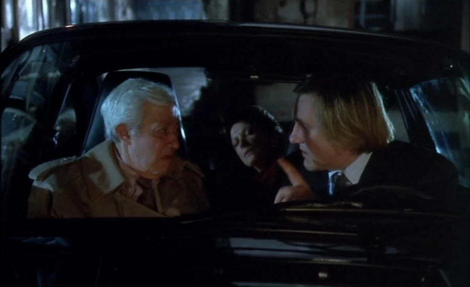 I Want To Go Home (1989) movie still: medium — The interior of a car at night with two men sitting in the front seats. The driver gestures with his…