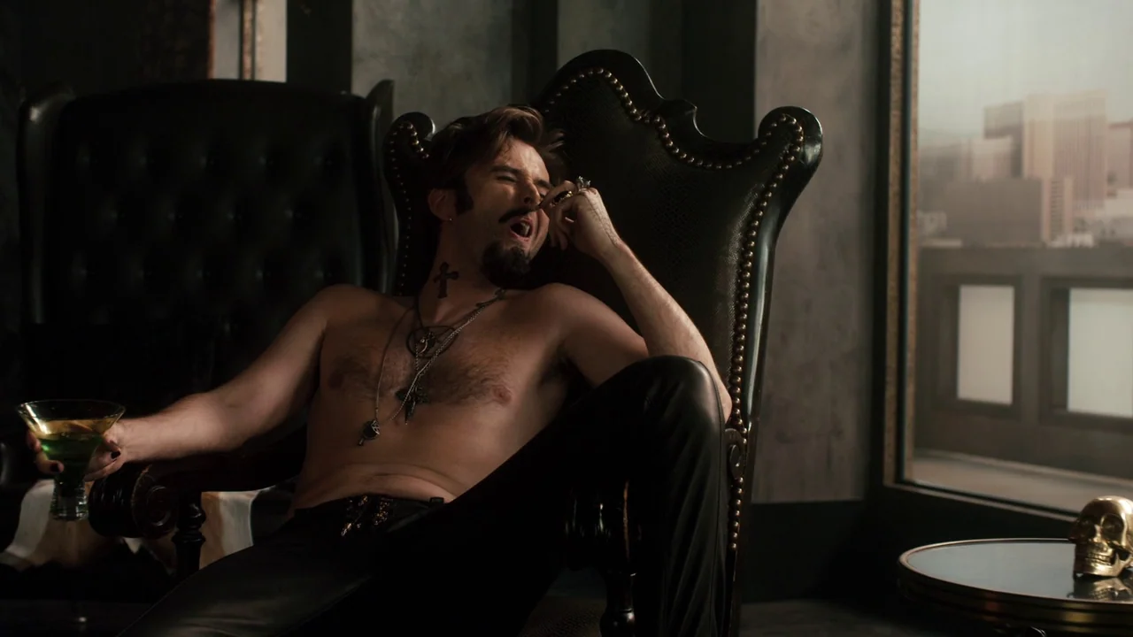 Fright Night (2011) movie still: medium — A dark, modern interior features a high-backed leather chair and a windowed view. A shirtless man with a…