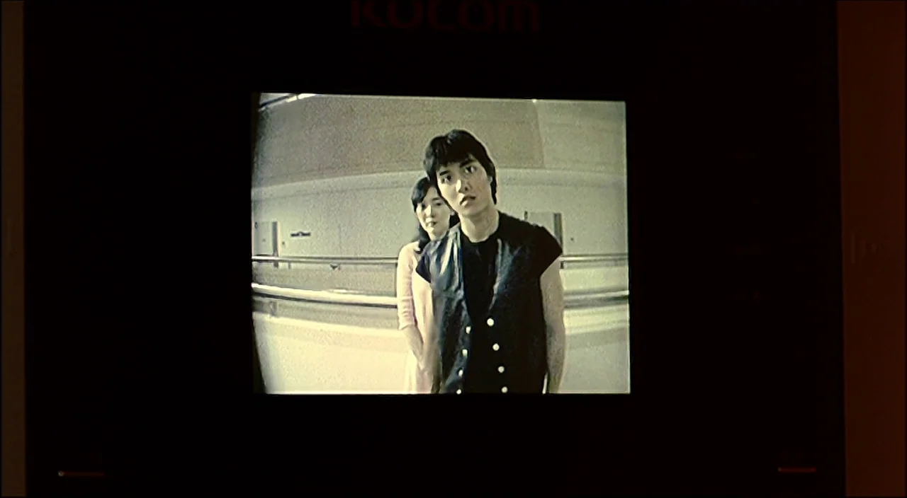 3-Iron (2004) movie still: medium — The image is seen through the low-resolution screen of a Kocom video intercom system. A man and a woman stand…