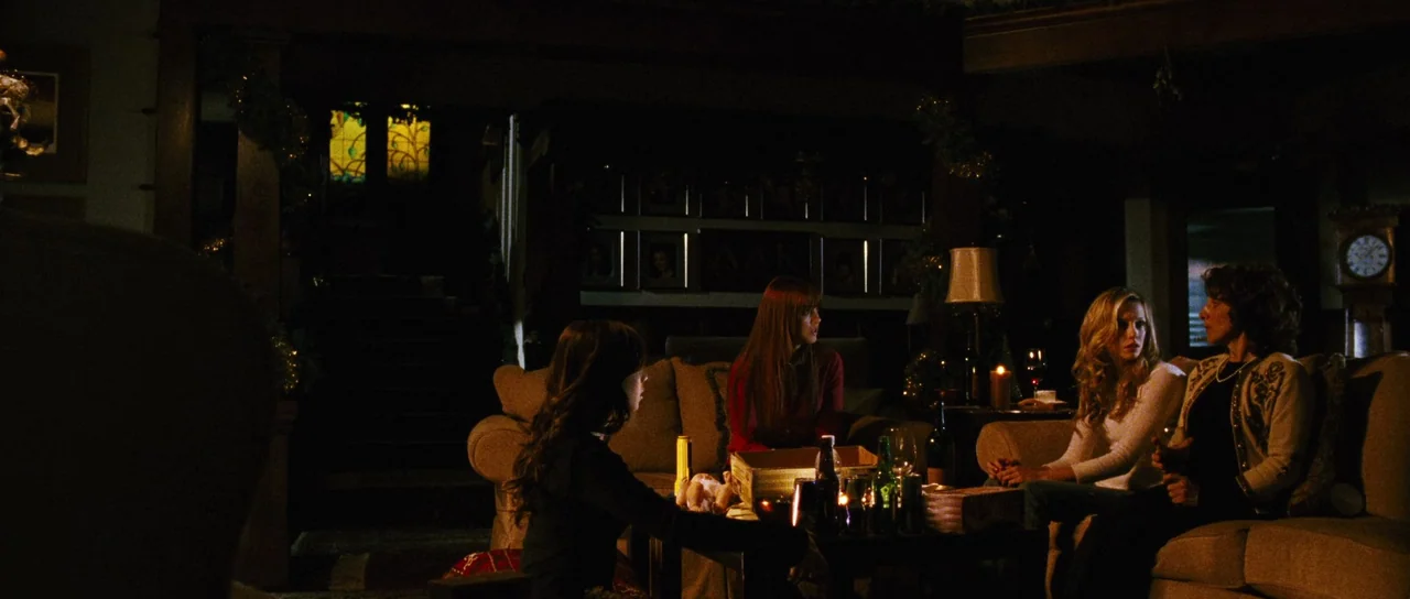 Black Christmas (2006) movie still: wide — A dimly lit room at night with several women sitting on beige upholstered couches. They are engaged in…