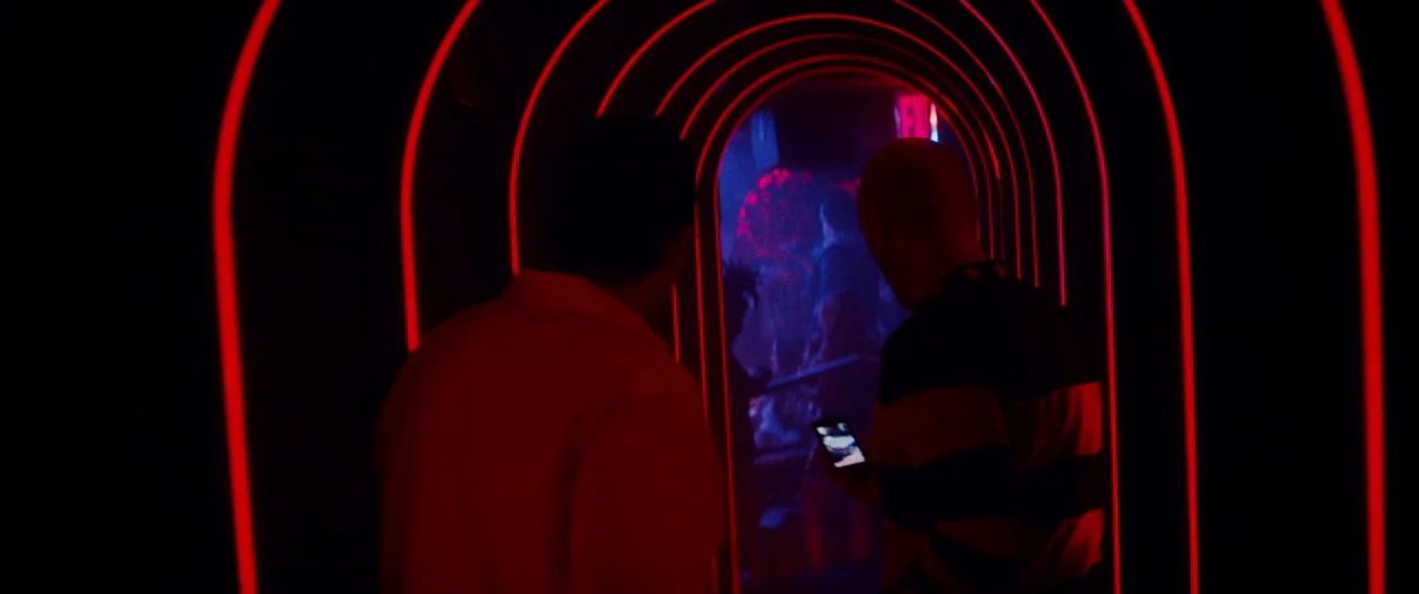Uncut Gems (2019) movie still: medium — A dark corridor is defined by concentric archways illuminated with bright red neon tubing. Two men walk…