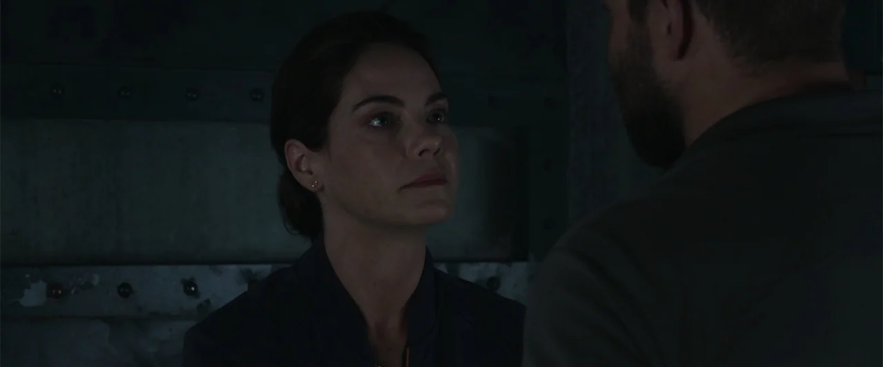 Black Site (2022) movie still: medium — A dimly lit interior space features dark walls with visible metal paneling details. A woman stands looking…