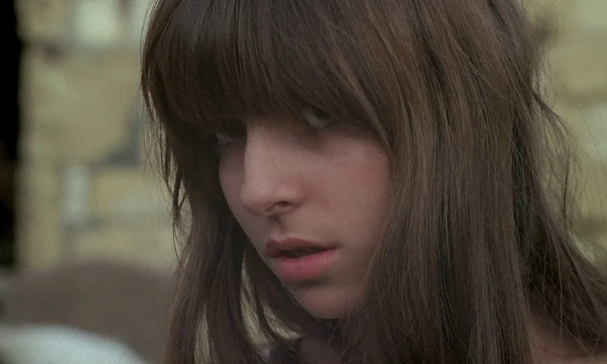 Immoral Tales (1974) movie still: closeup — A woman stands outdoors in a field with a blurred, light-colored background. She looks toward the camera…