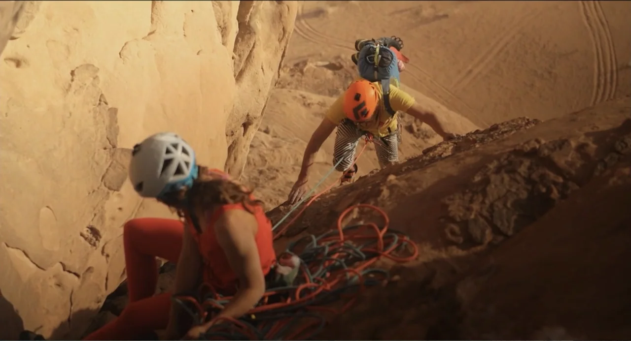 Crooked Trees Gon Give Me Wings (2022) movie still: medium — Two rock climbers navigate a steep sandstone cliff in a desert landscape. One climber…