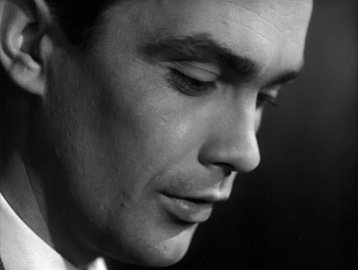 Thirst (1949) movie still: closeup — A close-up view of a man's profile in a dimly lit room. The subject looks down with a calm and steady expression.