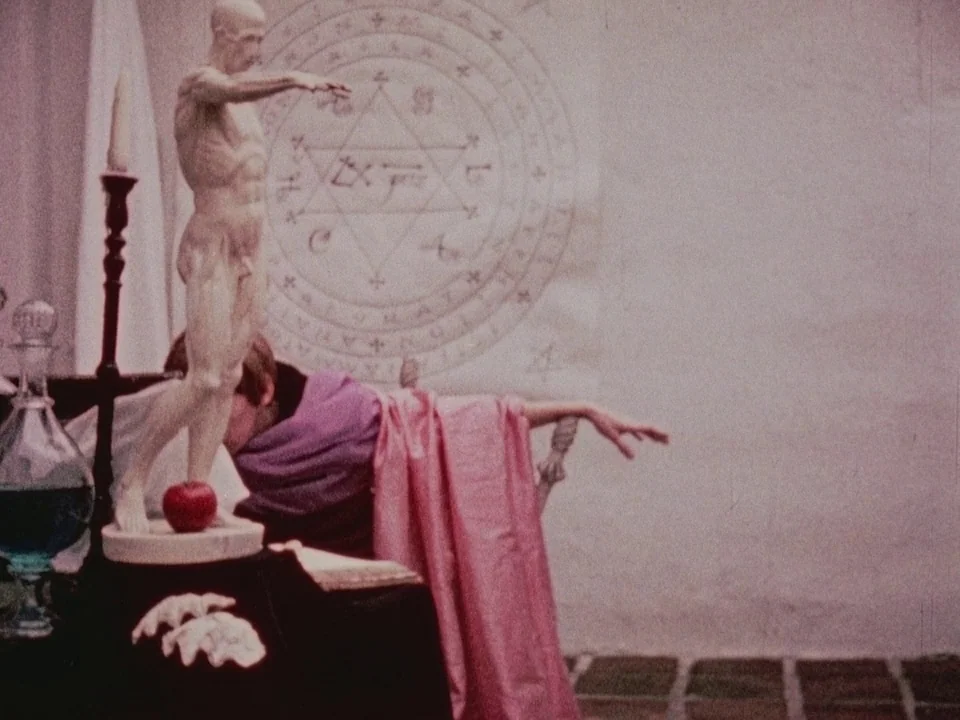 The Wormwood Star (1956) movie still: medium — A minimalist room features a large occult seal sketched on a white wall surface. A person draped in…