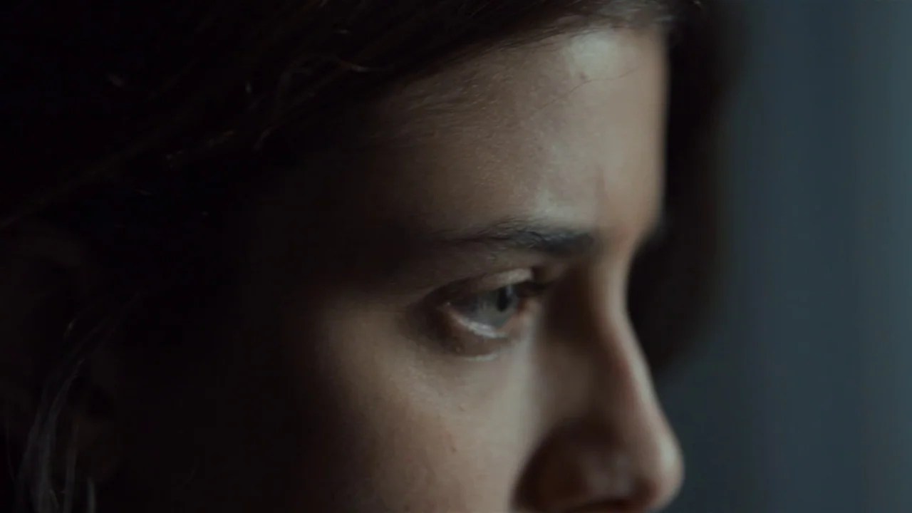 Amanda (2022) movie still: closeup — A close-up view shows a person's eye and temple in low light conditions. The subject is partially out of focus,…