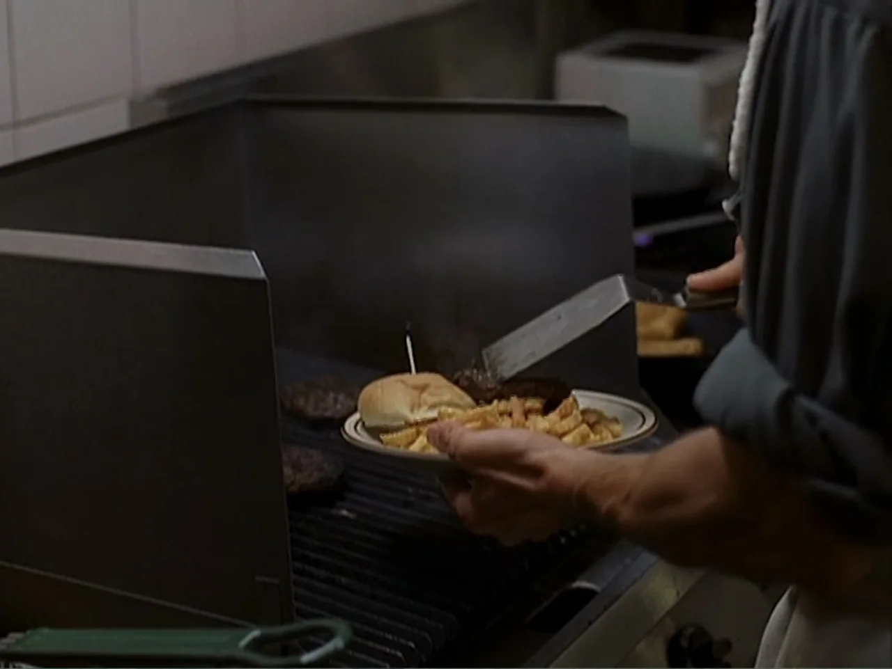 Catch a Falling Star (2000) movie still: medium — A stainless steel industrial grill sits inside a commercial kitchen with white tiled walls. A…