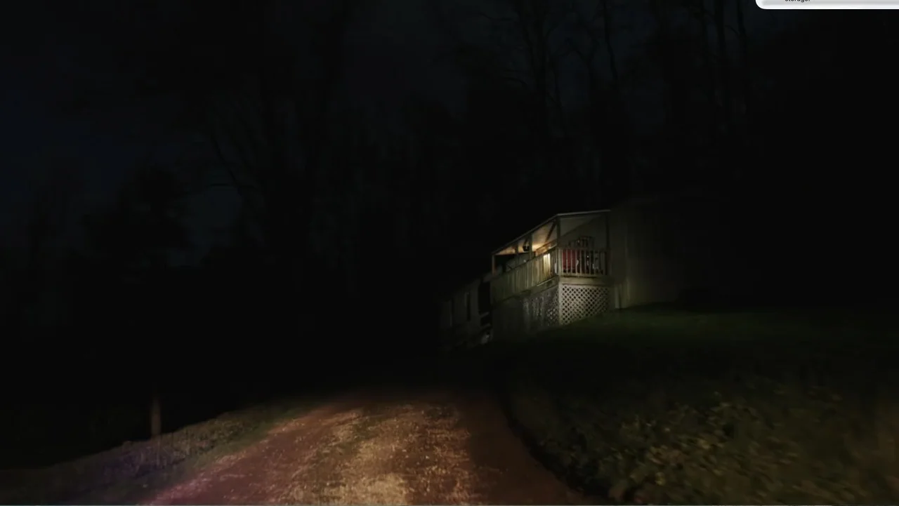 Murder at Carter County Mines (2023) movie still: wide — A dark rural road leads toward a mobile home with a lit front porch. The surrounding area…