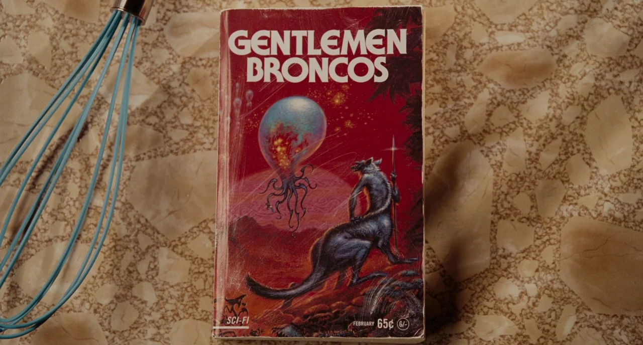 Gentlemen Broncos (2009) movie still: closeup — A science fiction paperback book sits on a speckled, beige terrazzo countertop. A light blue metal…
