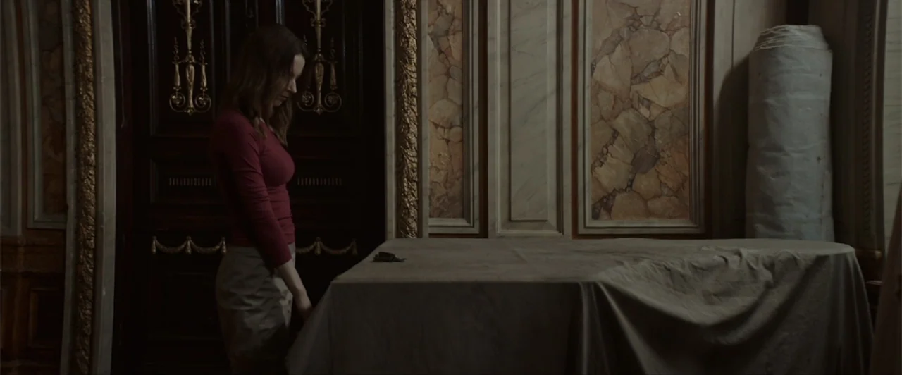 La herencia (2010) movie still: medium — A formal room features marble wall paneling and dark wood ornate doors. A woman stands in profile next to a…