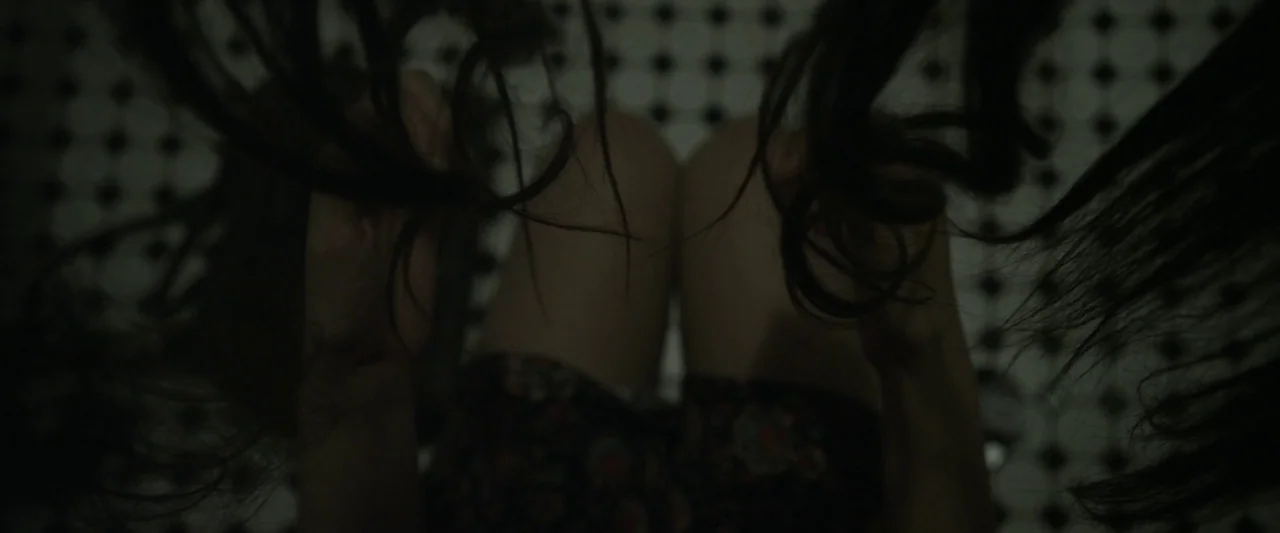 Starry Eyes (2014) movie still: closeup — A close-up of a person submerged in a basin with hexagonal black-and-white tiles. The subject's dark hair…