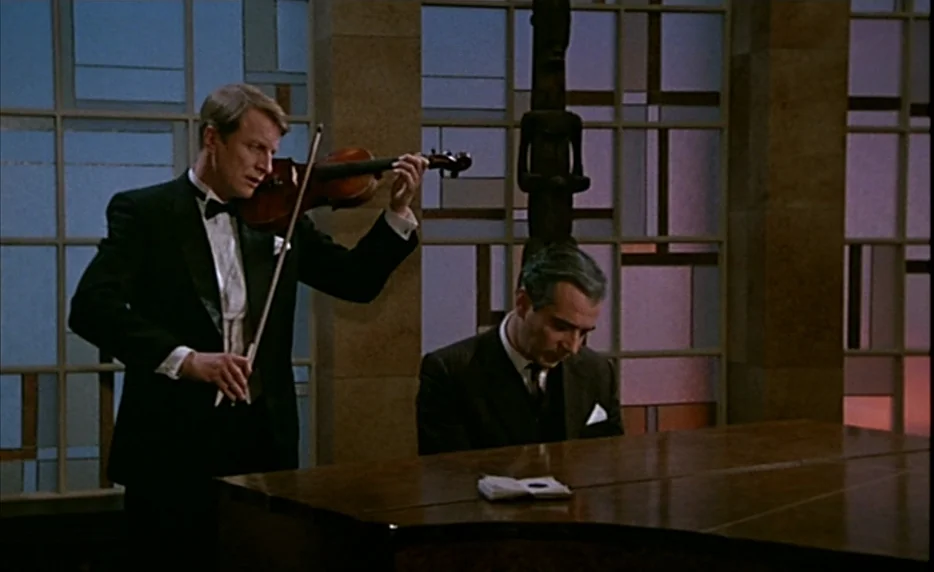 Mélo (1986) movie still: medium — A spacious room features floor-to-ceiling grid-patterned windows and a central wooden statuette. Two men in formal…