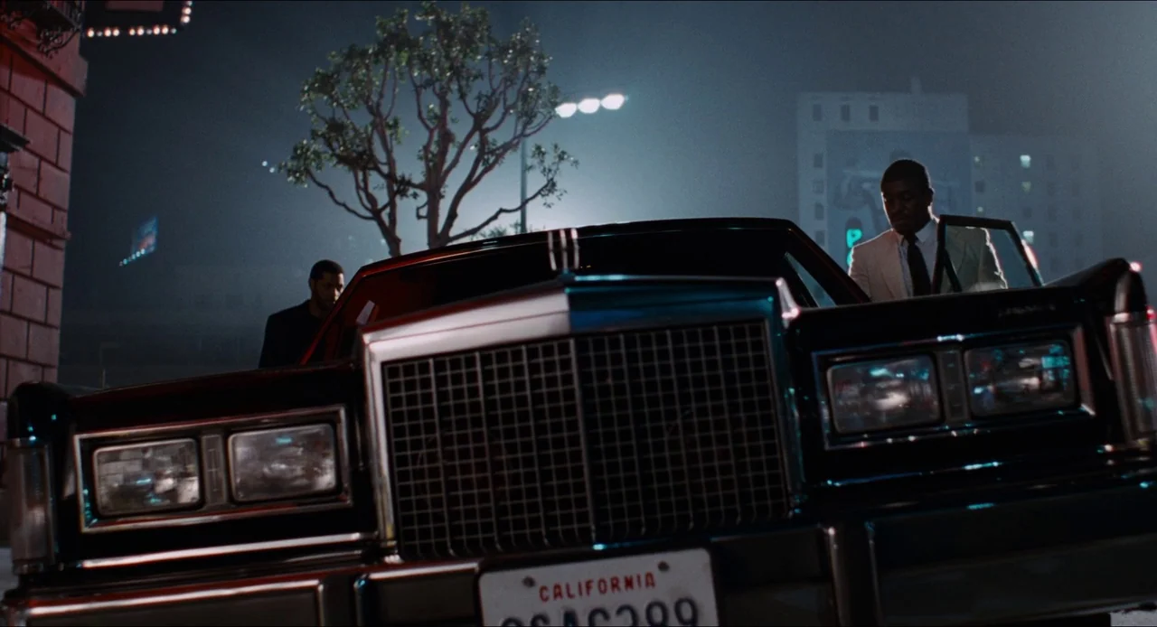 Deep Cover (1992) movie still: medium — A dark city street at night features a large black luxury sedan parked prominently. Two men in suits stand…
