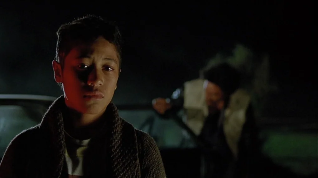 Boy (2010) movie still: medium — A dark night setting features a boy in the foreground and a blurred vehicle behind. An adult in a light vest works…