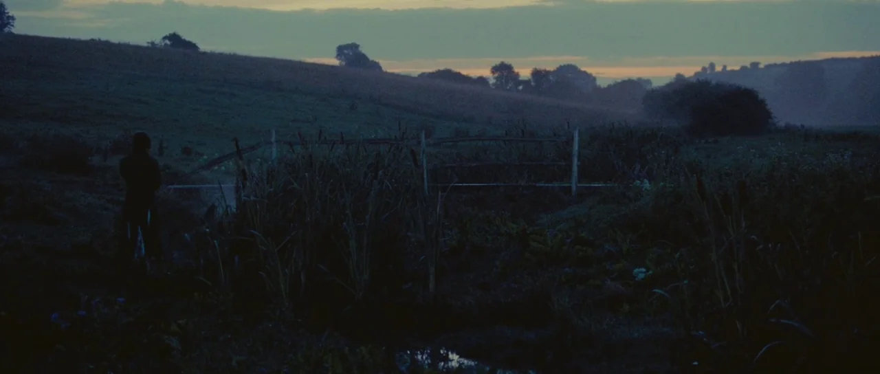Pride & Prejudice (2005) movie still: wide — A dark, expansive field during twilight features a wooden fence crossing the middle ground. A lone…