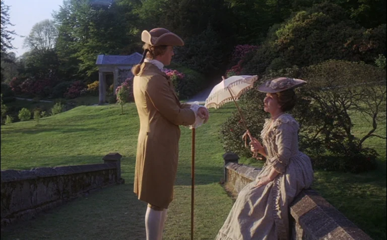 Barry Lyndon (1975) movie still: fullbody — A manicured park landscape with a stone bridge and a classical architectural structure behind. A man in…