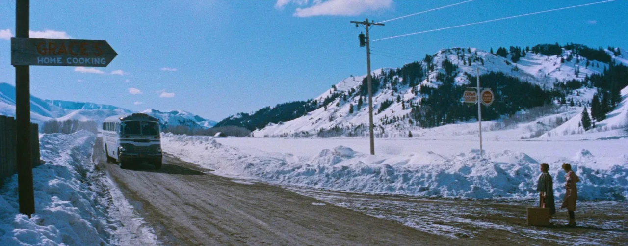 Bus Stop (1956) movie still: wide — A rural road bordered by thick snow banks winds through a mountain range. Two women stand on the dirt shoulder…