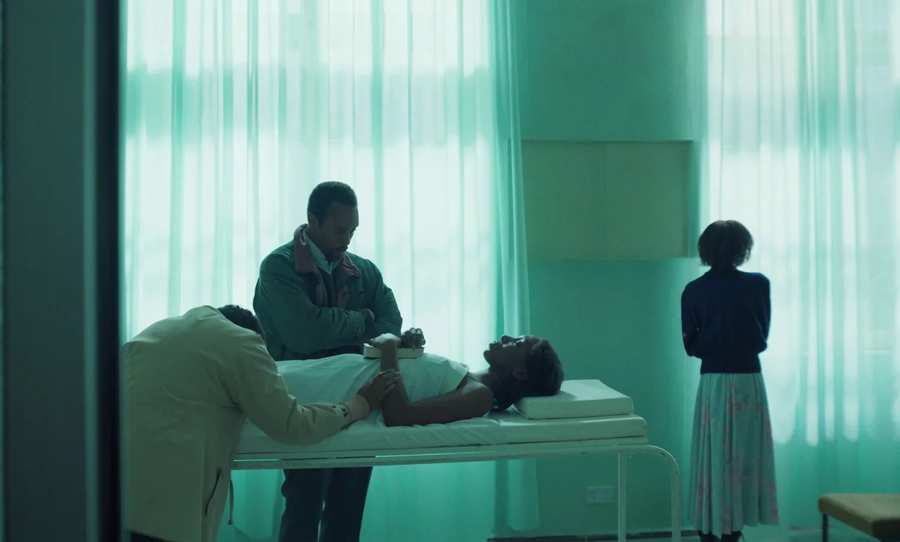 The Silent Twins (2022) movie still: medium — A sterile hospital ward features teal walls and translucent white curtains covering large windows.…