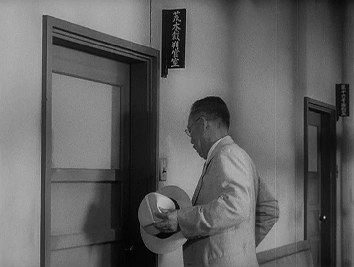 I Live In Fear (1955) movie still: medium — A quiet institutional hallway in a government building features plain walls and dark wooden doors. An…