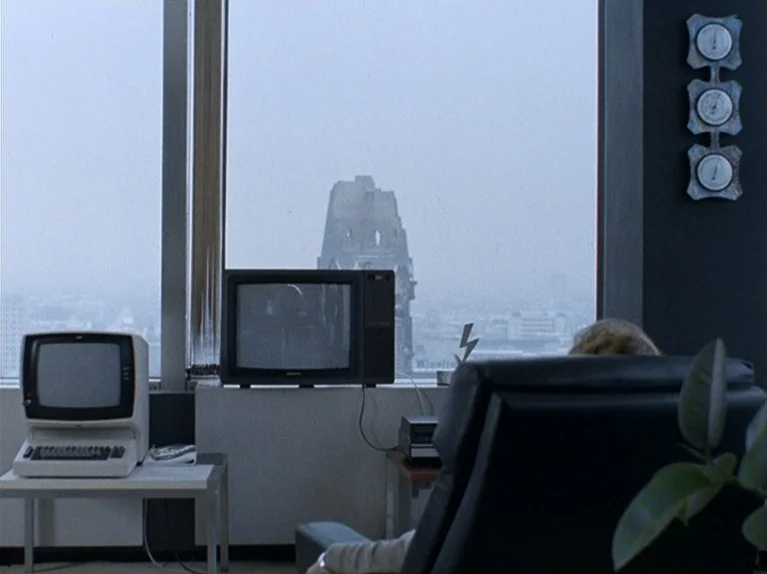 The Third Generation (1979) movie still: medium — A high-rise office with minimalist furniture overlooks a grey city skyline. A person sits in a…
