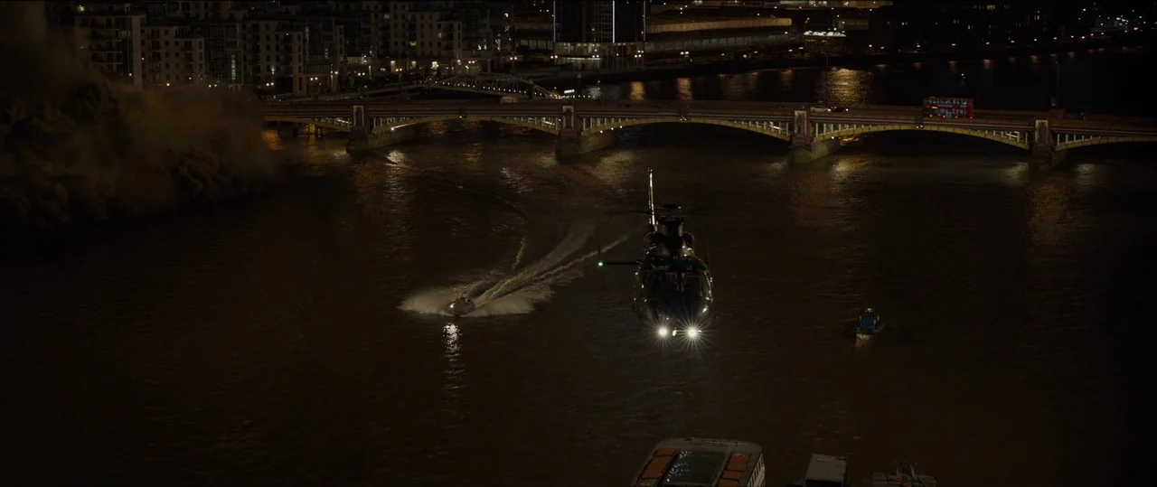 Spectre (2015) movie still: wide — A nighttime aerial view shows a helicopter hovering over the Thames river in London. A speed boat navigates the…