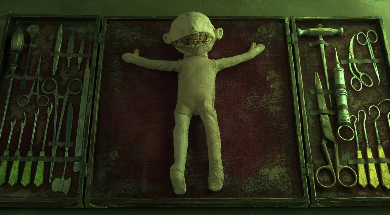 Coraline (2009) movie still: wide — A dark red velvet-lined surgical display case contains a worn, stitched cloth doll. The doll is positioned in…