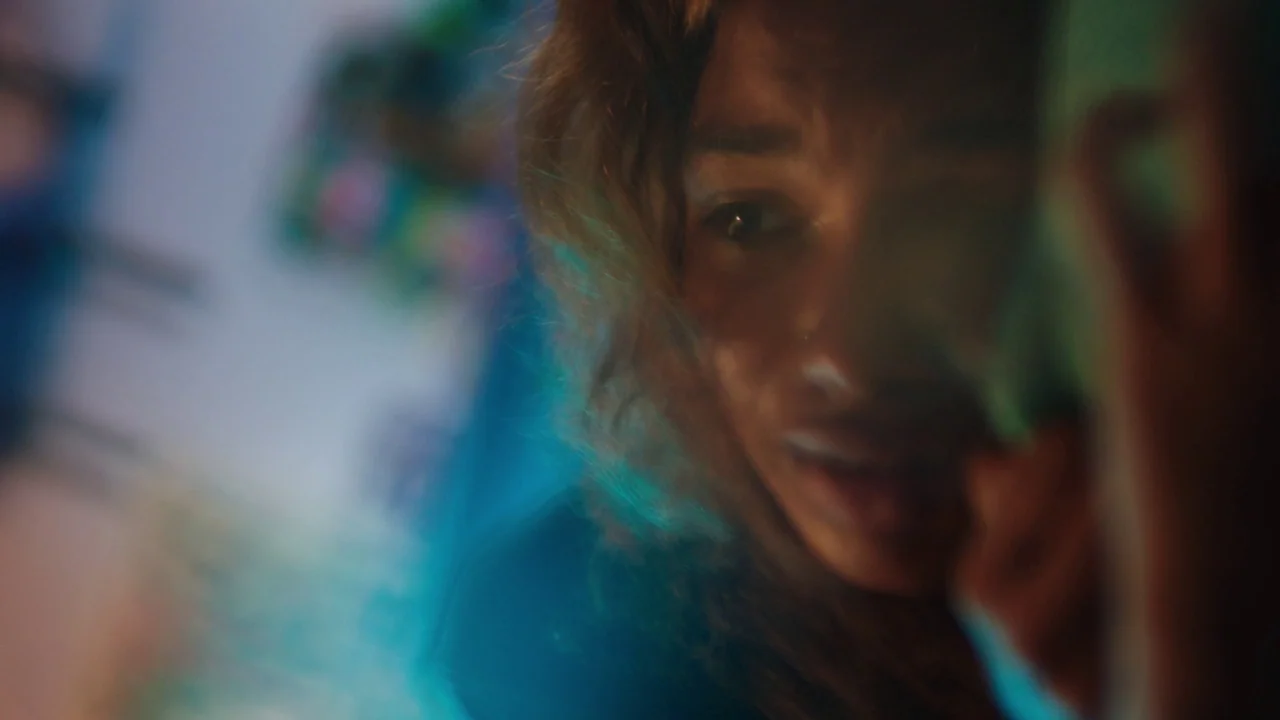 Madeline’s Madeline (2018) movie still: closeup — A close-up of a person in a dark room illuminated by a blue glow. The subject focuses their gaze…