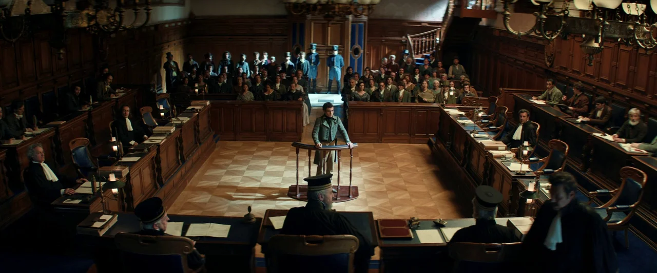 The Count of Monte-Cristo (2024) movie still: wide — A high-angle view of a formal 19th-century courtroom with ornate wood paneling. A young man…