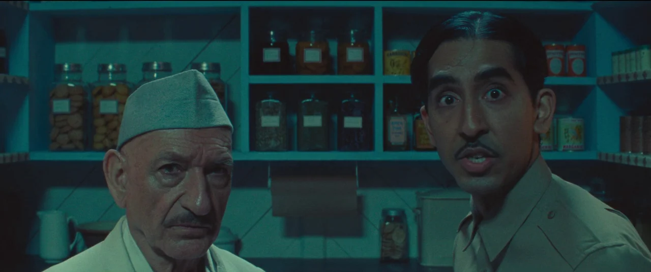 Poison movie still: medium — A dark pantry with wooden shelves filled with glass jars of food items. Two men stand in the foreground, illuminated by…