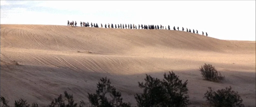 Three Kings (1999) movie still: wide — A vast, undulating expanse of beige desert sand features gentle slopes and visible tire tracks. A long, thin…