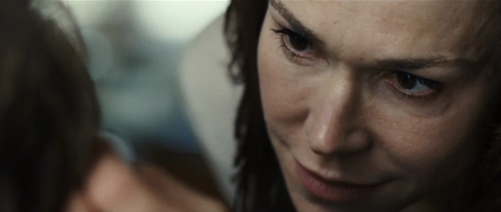 The Hunter (2011) movie still: closeup — A close-up view shows a woman interacting with another person in an interior space. The woman stares at the…