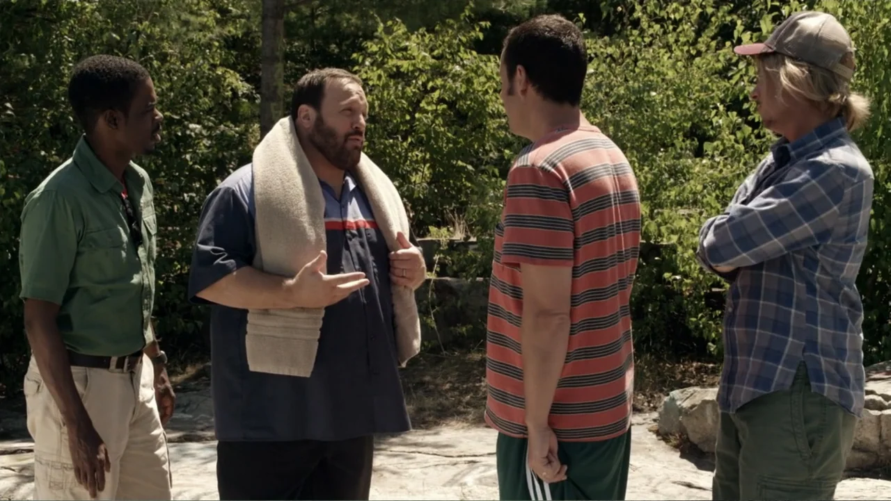 Grown Ups 2 (2013) movie still: medium — A sunny wooded area with dense green foliage and rocky ground. Four men stand in a small cluster conversing…
